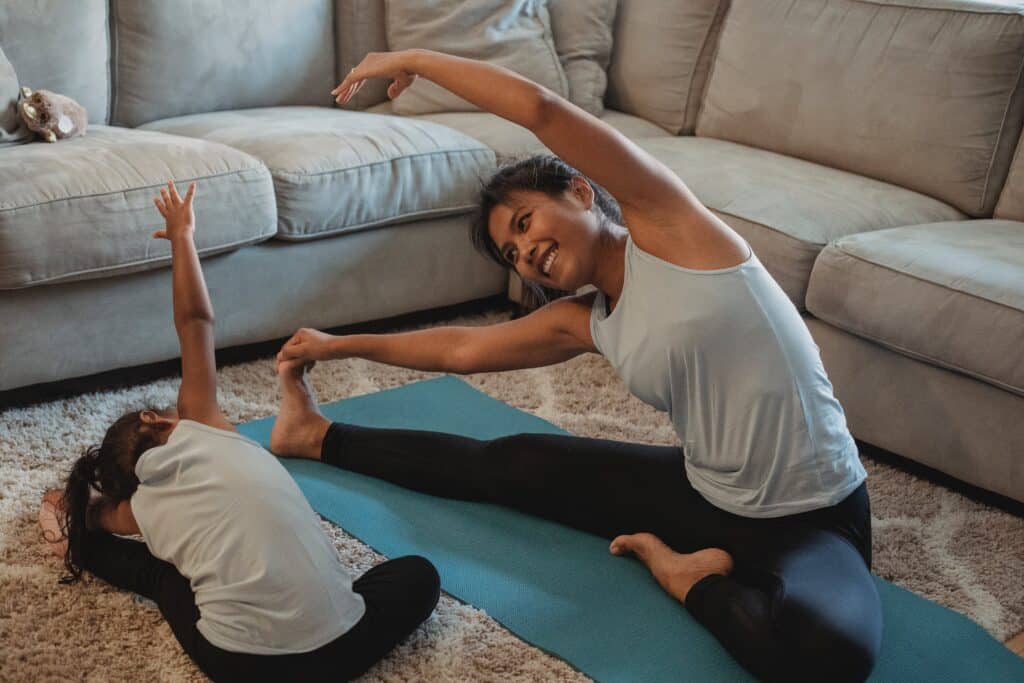 A mother in addiction recovery doing stretching exercises with her young daughter.