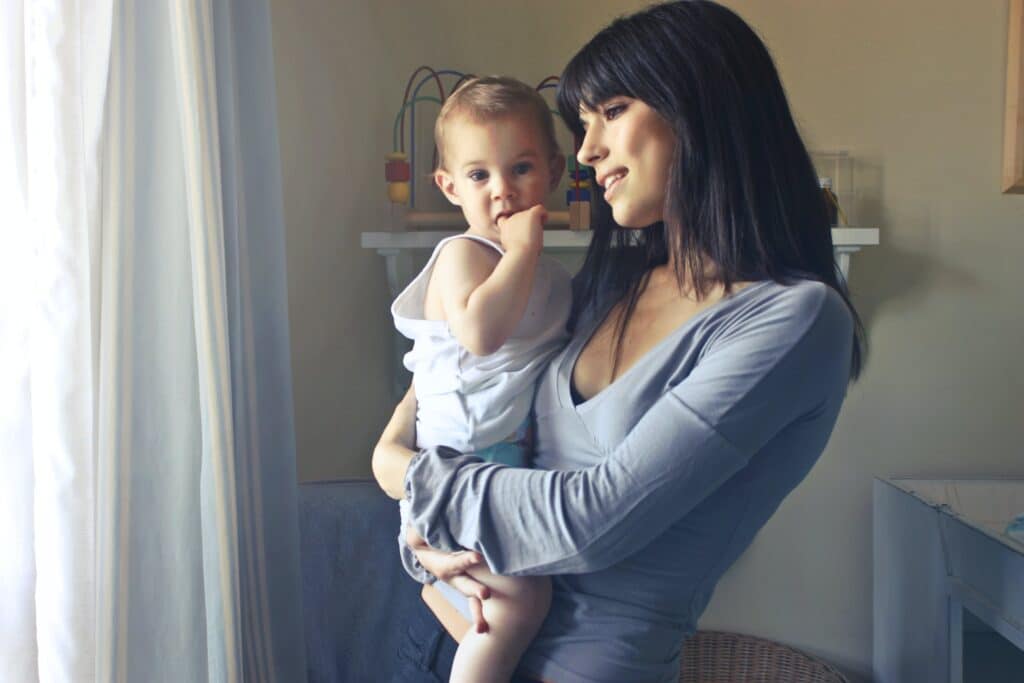 A mother in addiction recovery holding her baby in her arms, looking out a window.