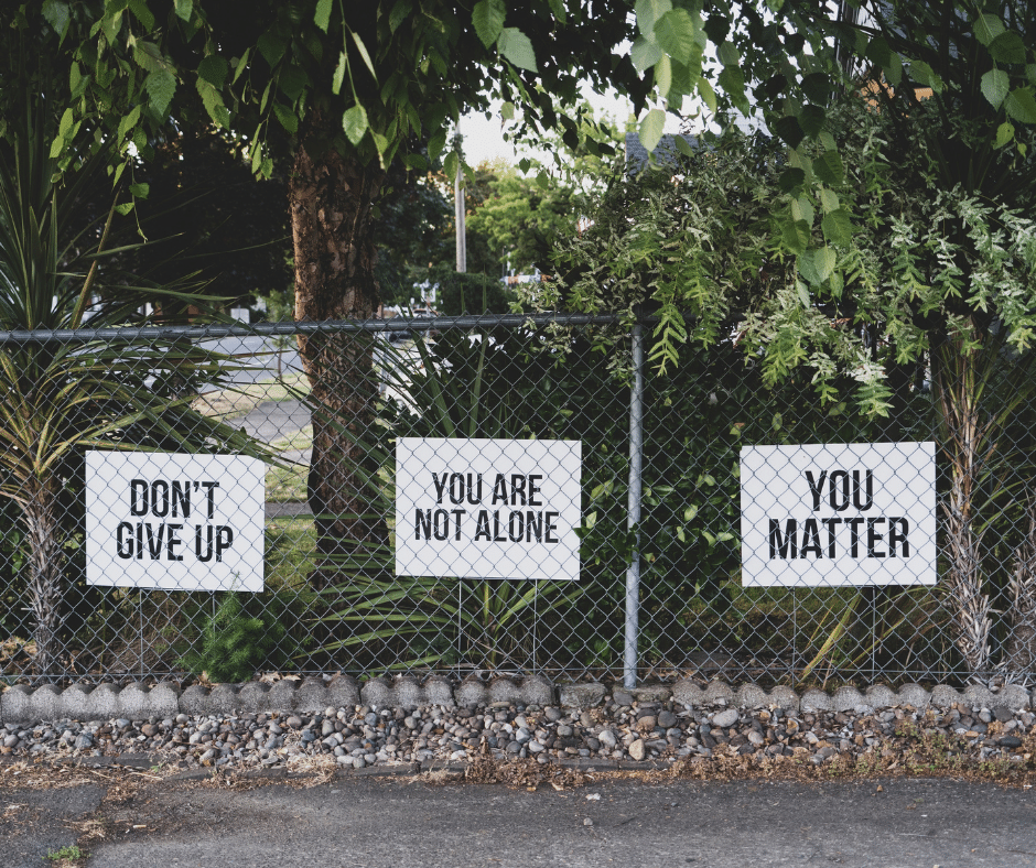 Fence by trees with 3 white signs: 'Don't Give Up', 'You Are Not Alone', and 'You Matter'.