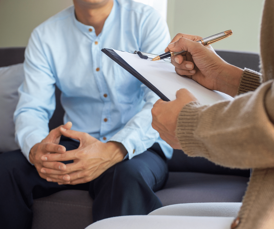 Man in discussion with a counselor, who is taking notes on a clipboard during a counseling session.
