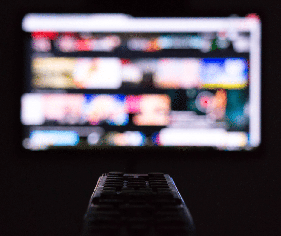 TV remote in the foreground with a glowing television screen in the background.