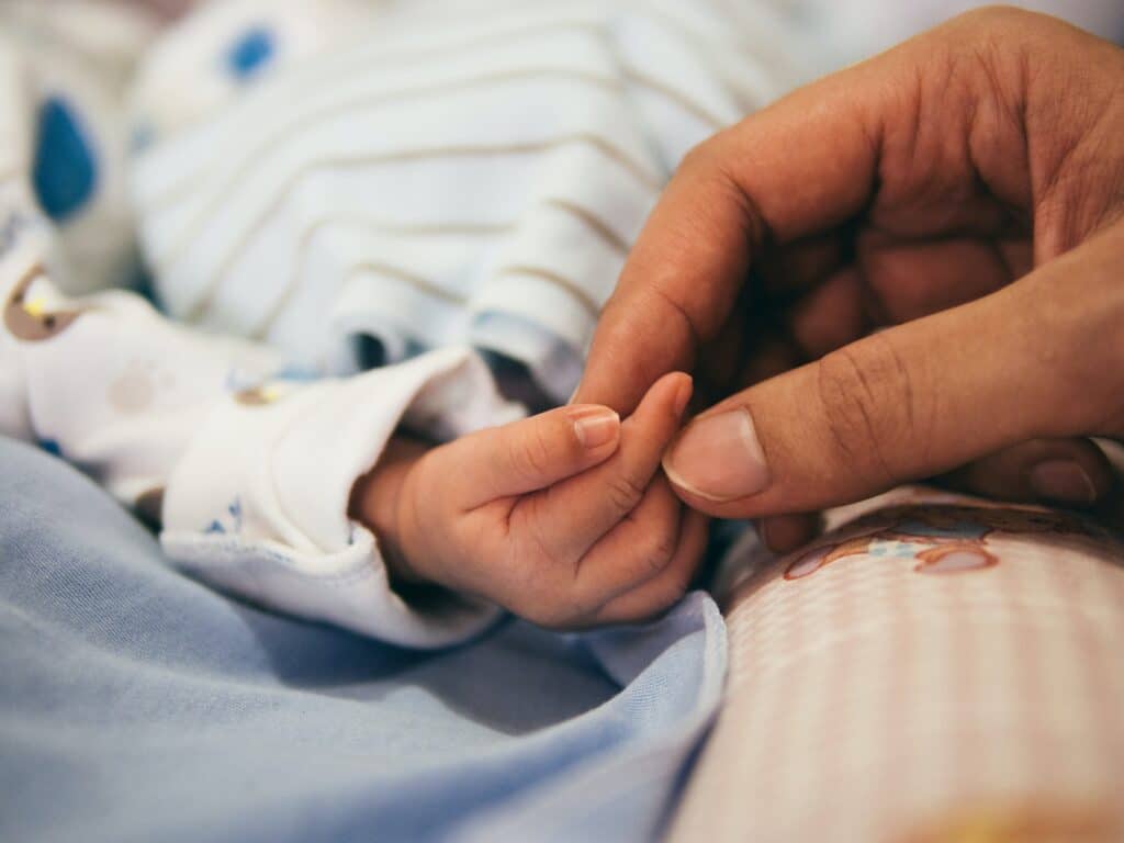 Adult hand tenderly holding a newborn's tiny hand, symbolizing care and protection in the early stages of life.