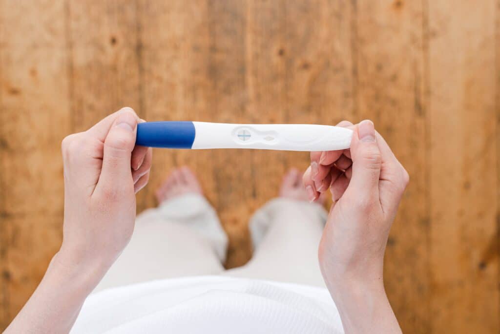 A woman looking down at a positive pregnancy test, symbolizing the challenging journey ahead for those struggling with opioid addiction during pregnancy.