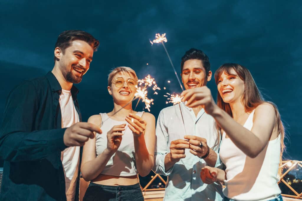 A joyful group of friends on a rooftop, smiling and holding sparklers, celebrating the New Year together.