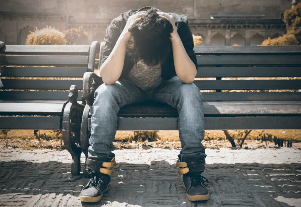 A man sitting on a bench with his head in his hands, depicting a moment of struggle potentially related to relapse.